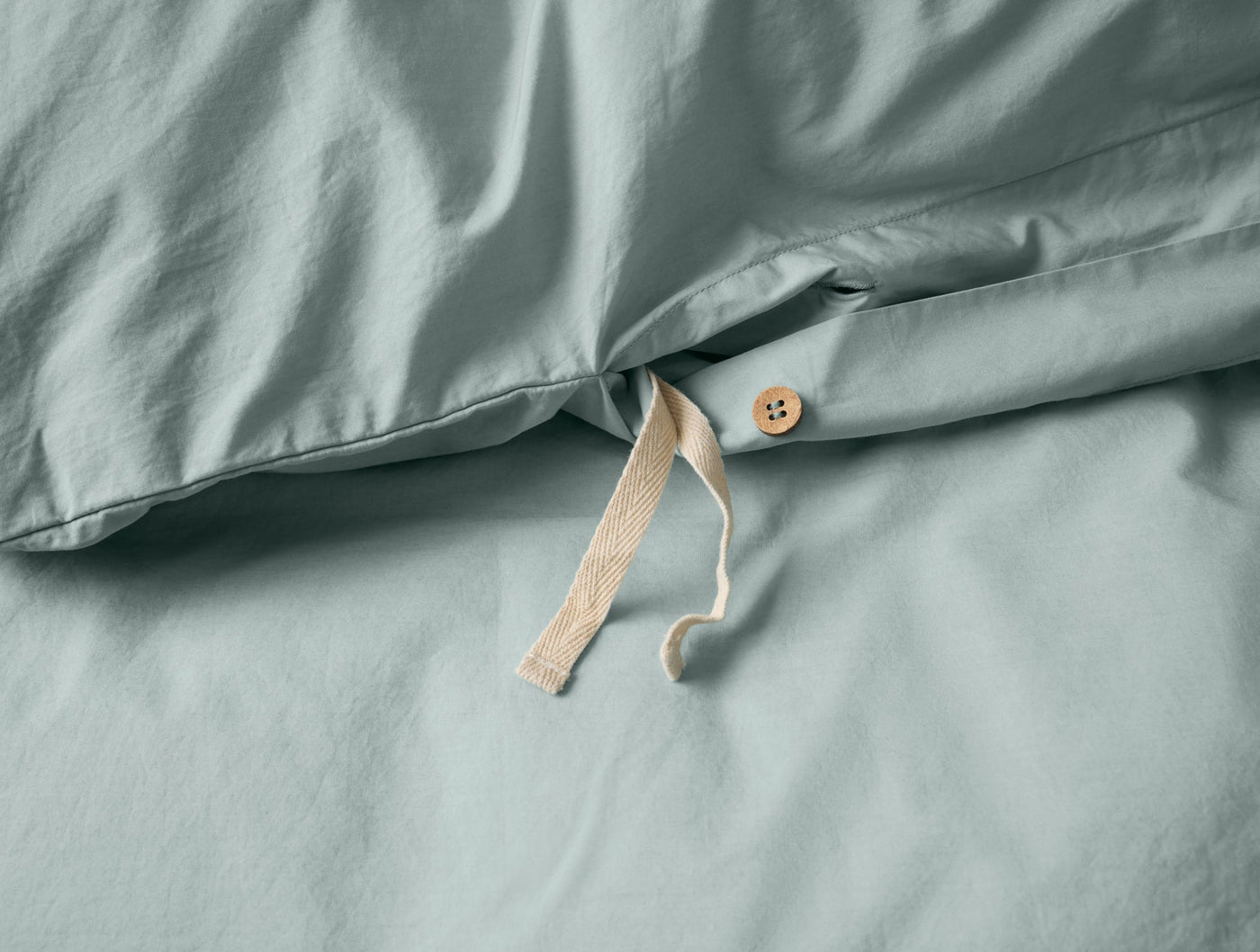 Close-up of sage percale duvet cover closure with natural cotton ties and wood button.