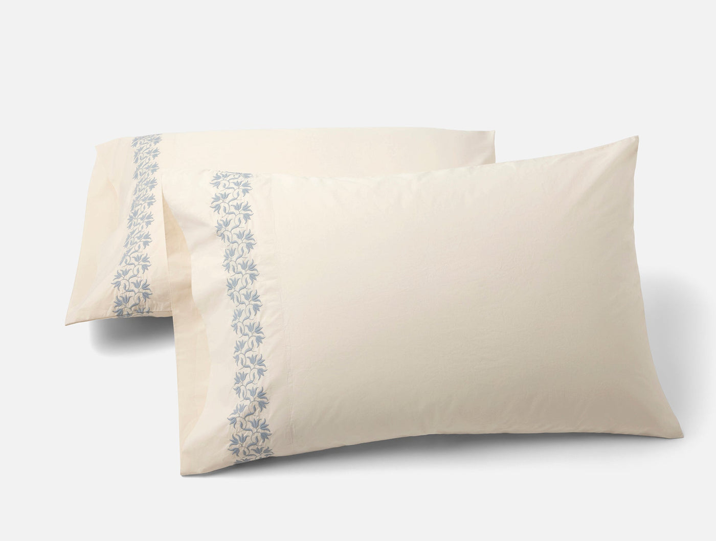 Pair of ivory Coyuchi Refined Percale pillowcases with blue floral embroidered border trim.