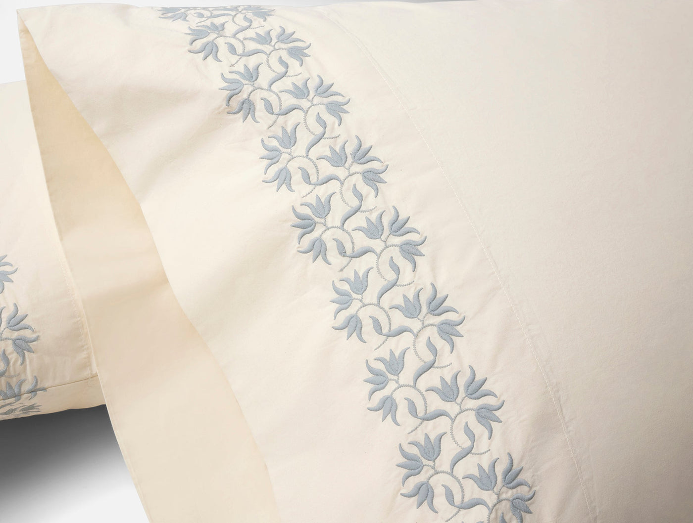 Close-up of blue floral embroidered border trim on ivory Coyuchi Refined Percale sheets.