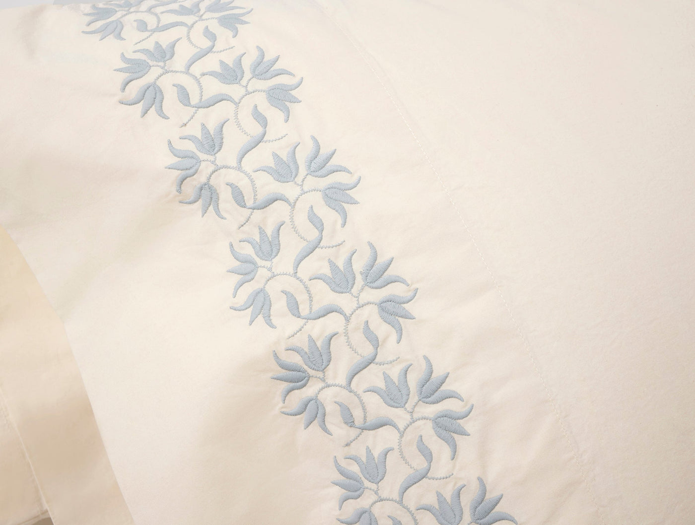 Close-up of powder blue floral embroidered border on ivory percale pillowcase.