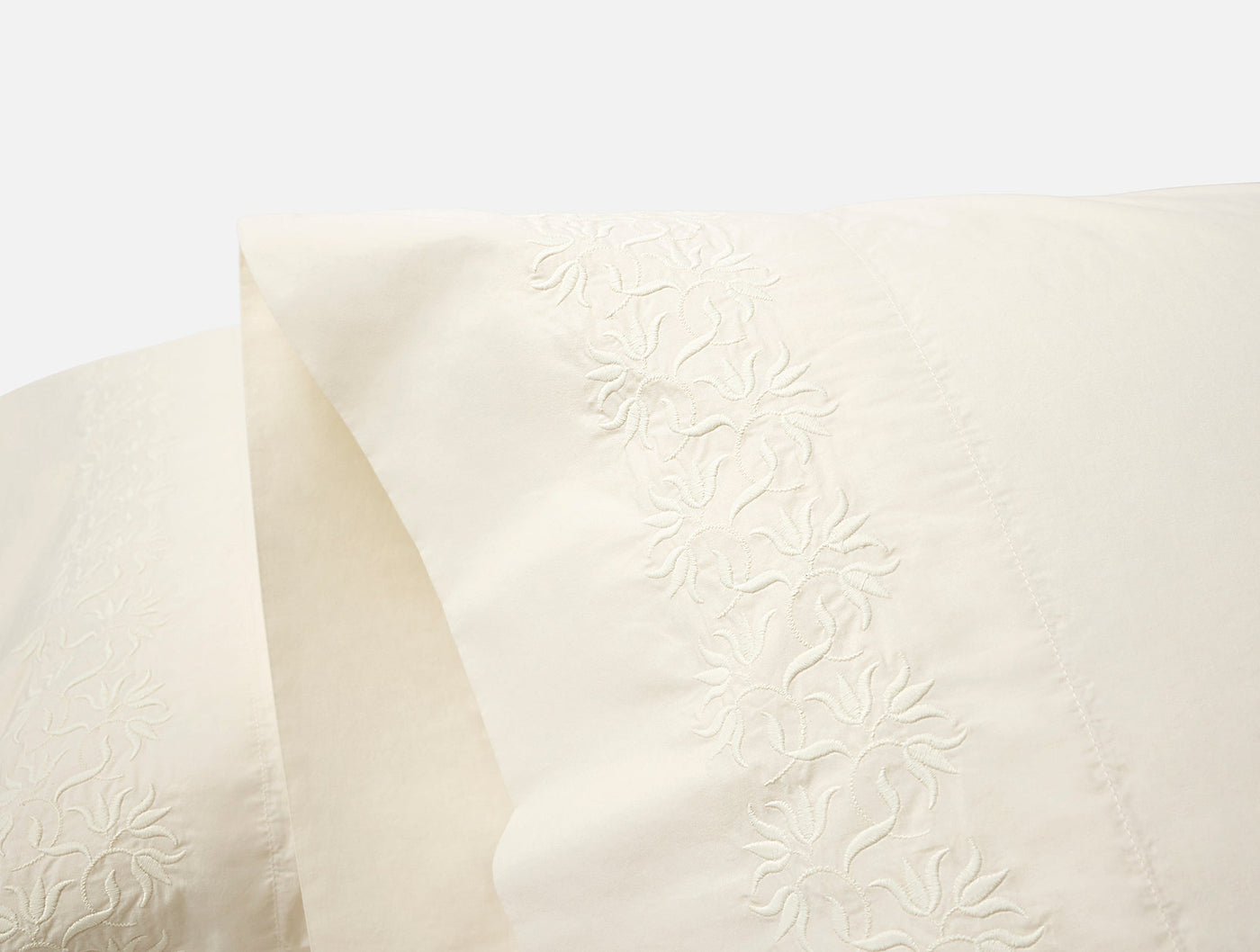 Close-up of ivory percale pillowcase hem with tonal floral embroidery detail.