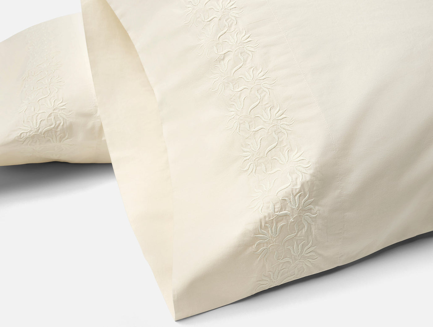 Close-up of embroidered floral hem detail on ivory Coyuchi Refined Percale pillowcases.