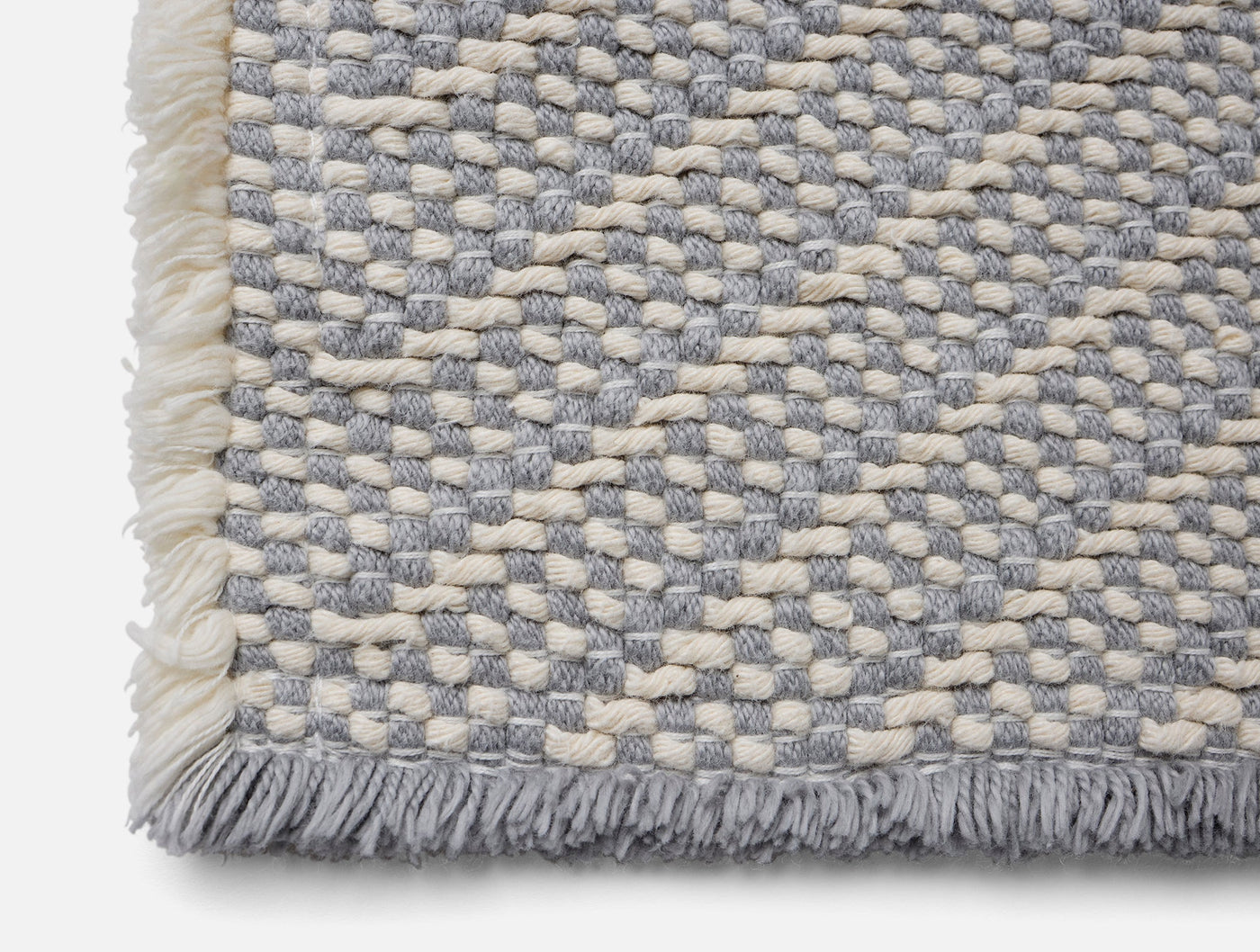 Close-up corner of Coyuchi Ridge bath rug showing slate and ivory woven texture with fringe.