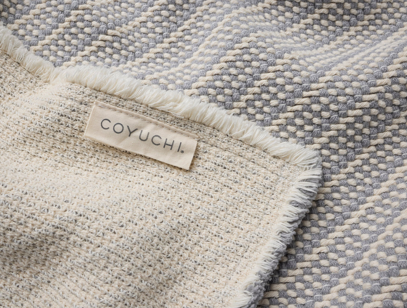 Coyuchi Ridge bath rug close-up showing woven texture, fringe edge, and fabric label.
