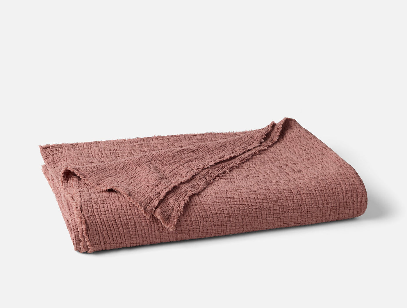 Folded Coyuchi Topanga Matelassé blanket in dusty rose with textured weave and fringe edge.