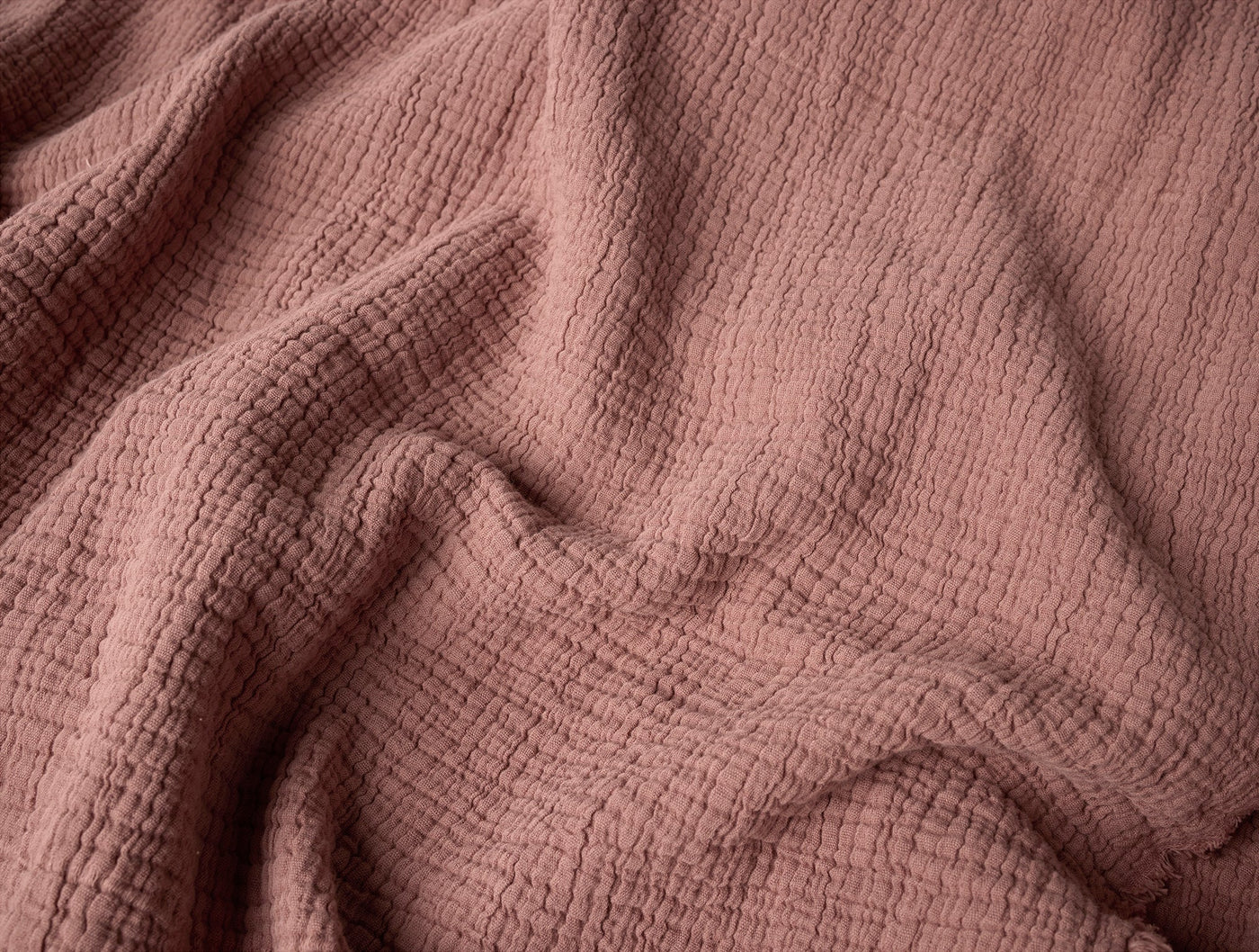 Close-up of Coyuchi Topanga Matelasse blanket in dusty rose, showing crinkled cotton texture.