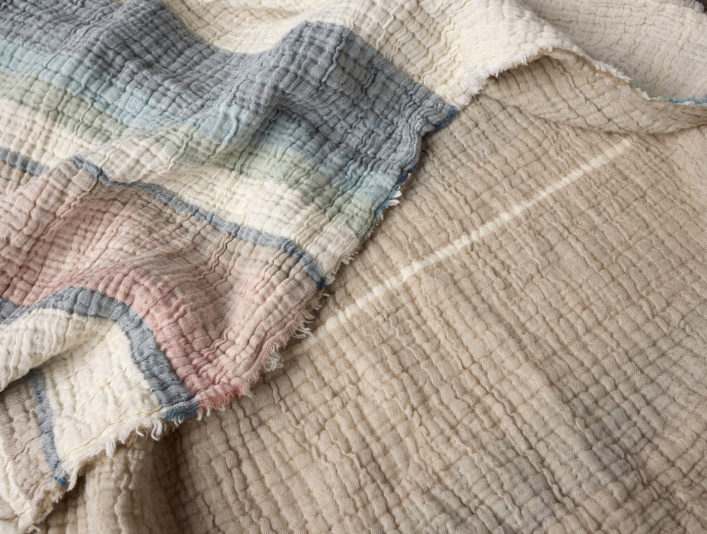 Close-up of Coyuchi Topanga Matelassé throw, showing frayed edge detail in soft blue, blush, and sand stripes.