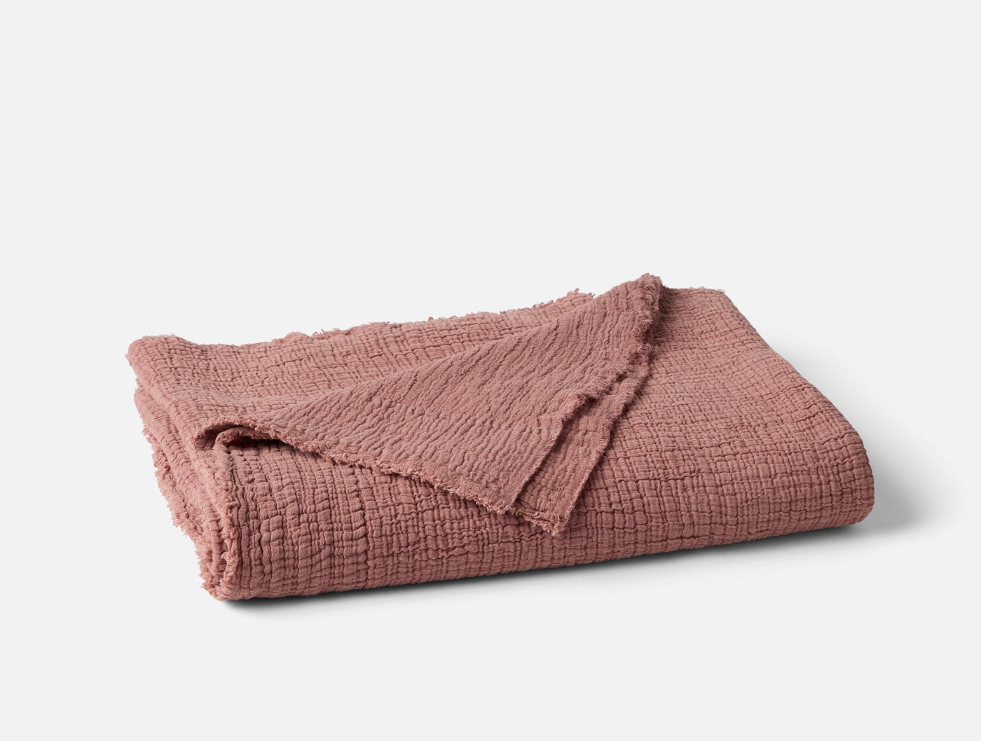 Folded rose Coyuchi Topanga Matelasse throw showing textured weave and frayed edges.