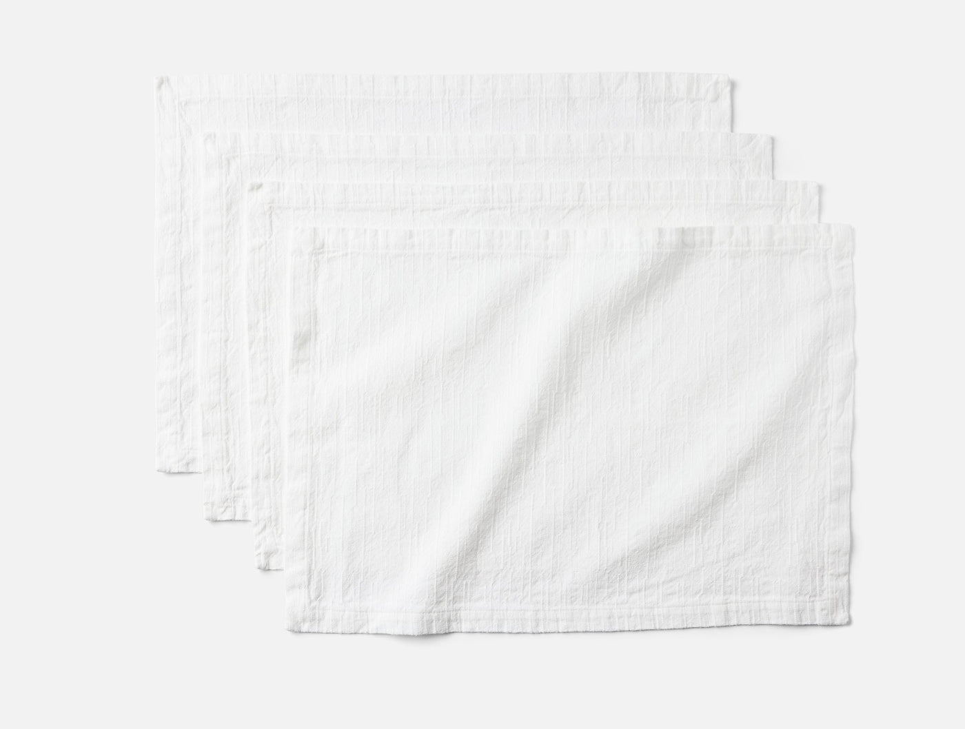 Coyuchi Toro Canyon placemats in white, set of four fanned on grey background.