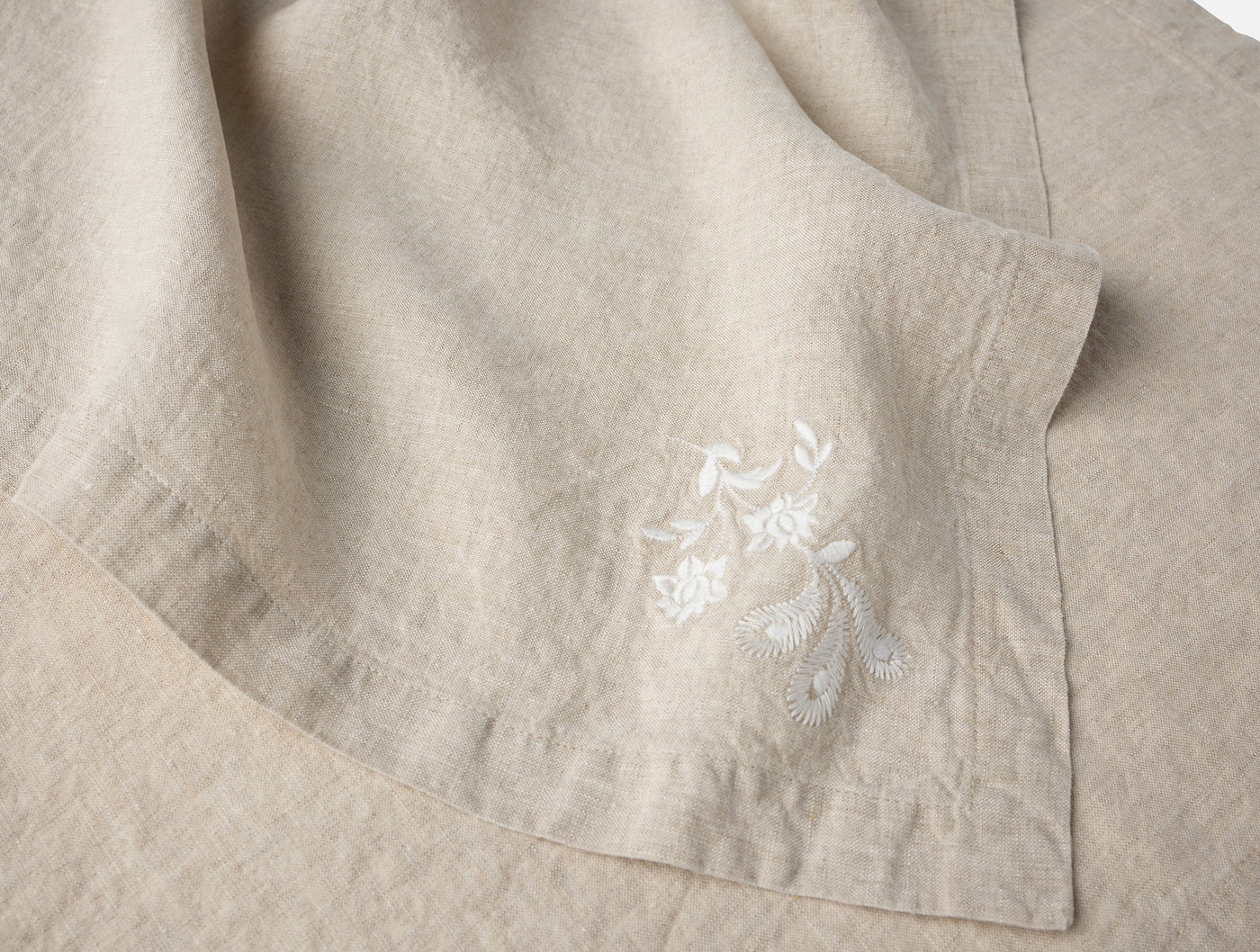 Close-up of natural linen napkin corner with white floral embroidery detail.