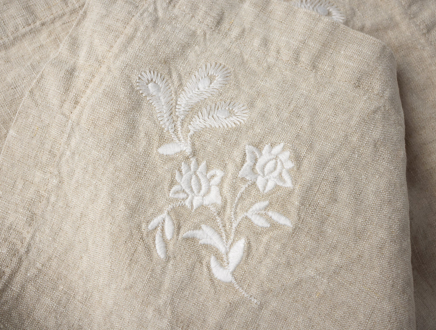 Close-up of white floral embroidery on a folded natural linen napkin corner.