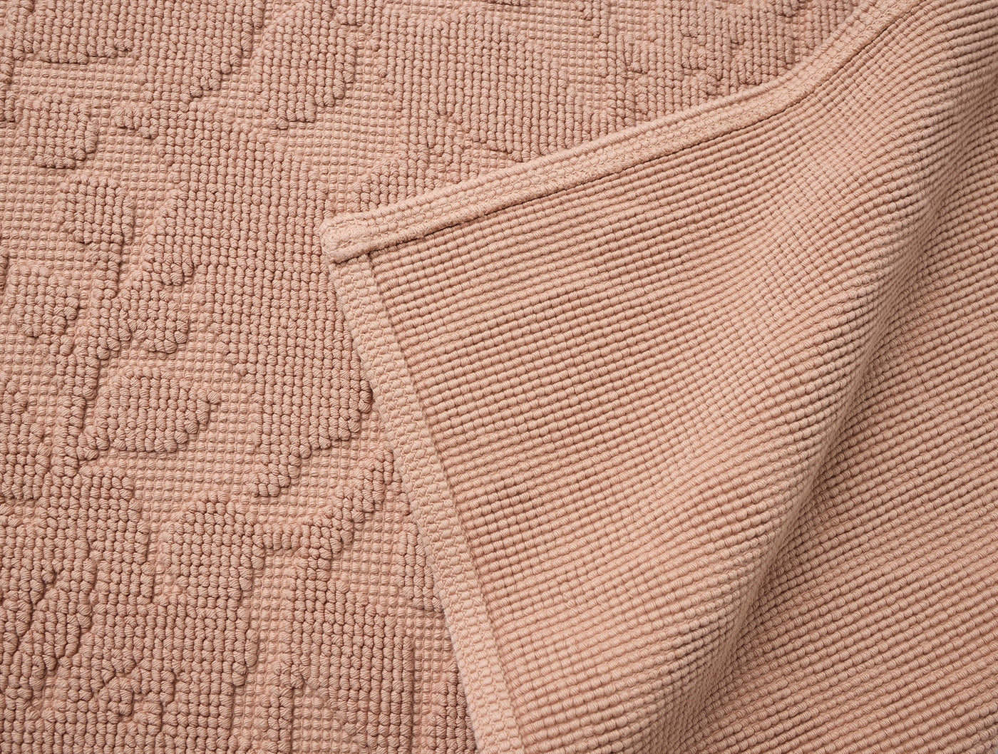 Corner fold detail of Coyuchi Wildflower bath rug in blush, showing floral texture and waffle reverse.