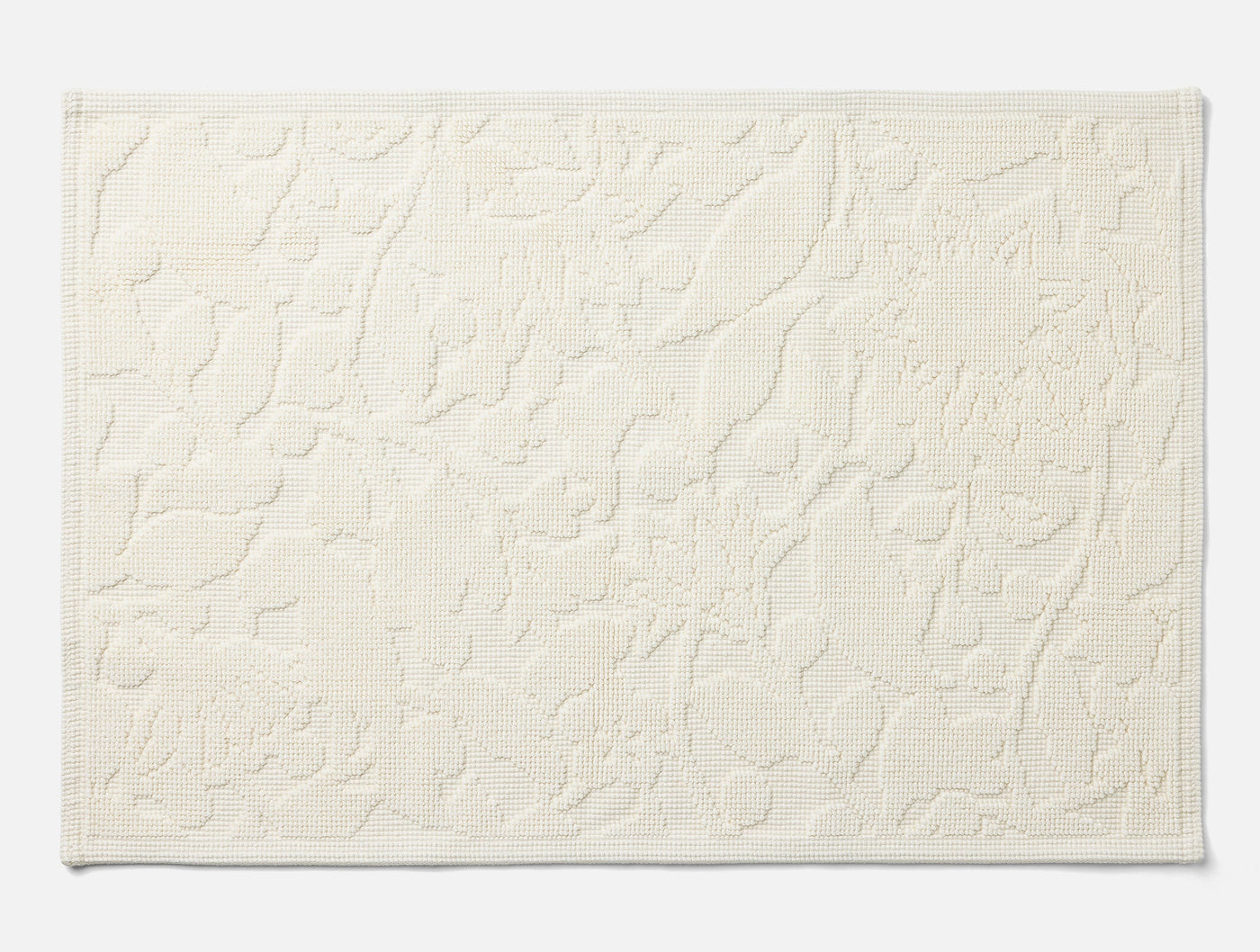 Coyuchi Wildflower bath rug in ivory, flat lay showing embossed floral texture detail.