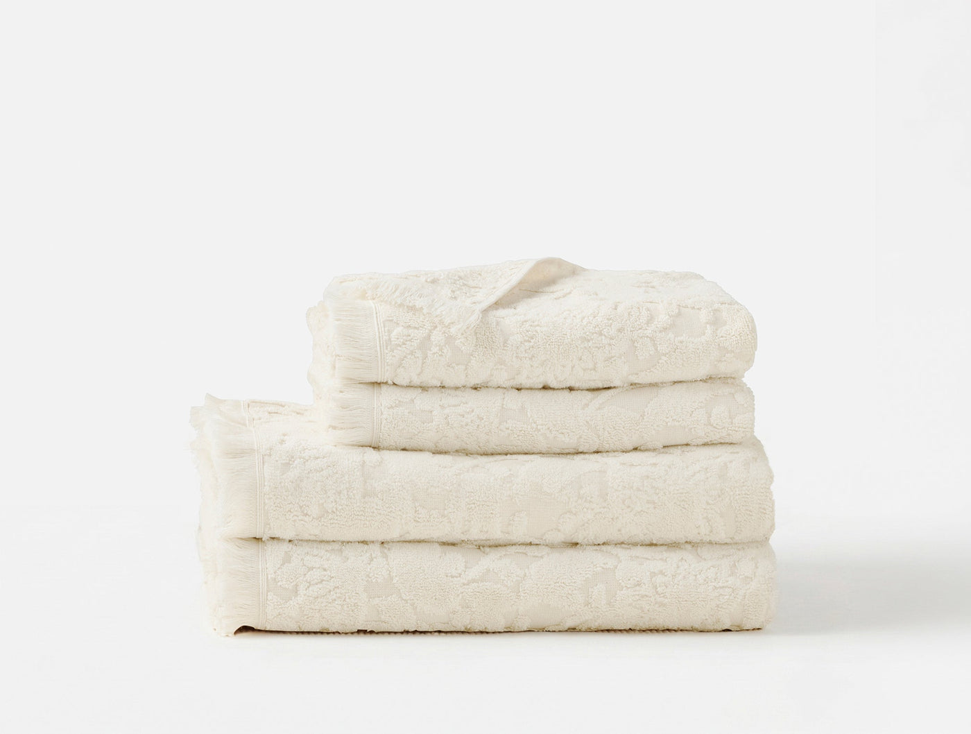 Stack of four ivory Coyuchi Wildflower towels showing jacquard floral texture, folded neatly.