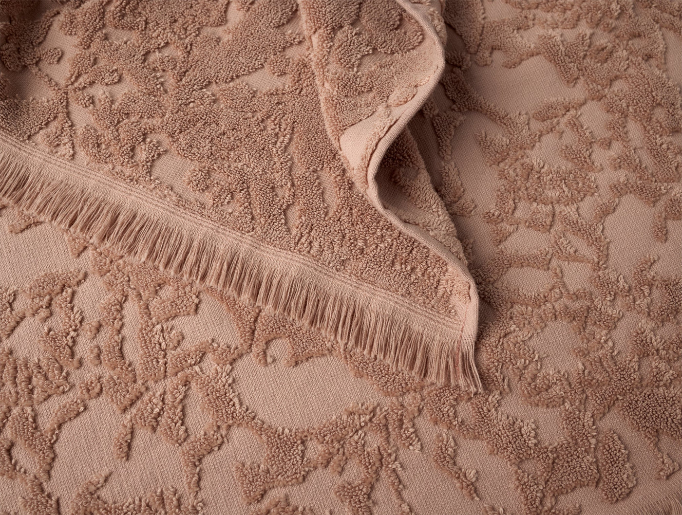 Close-up of Coyuchi Wildflower bath towel in clay, showing floral terry texture and fringe hem detail.