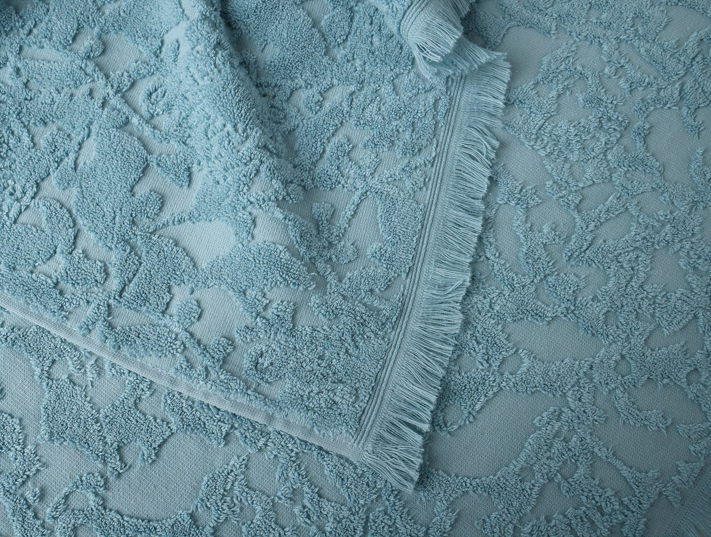 Close-up of Coyuchi Wildflower hand towel in sky blue showing floral terry texture and fringe trim.