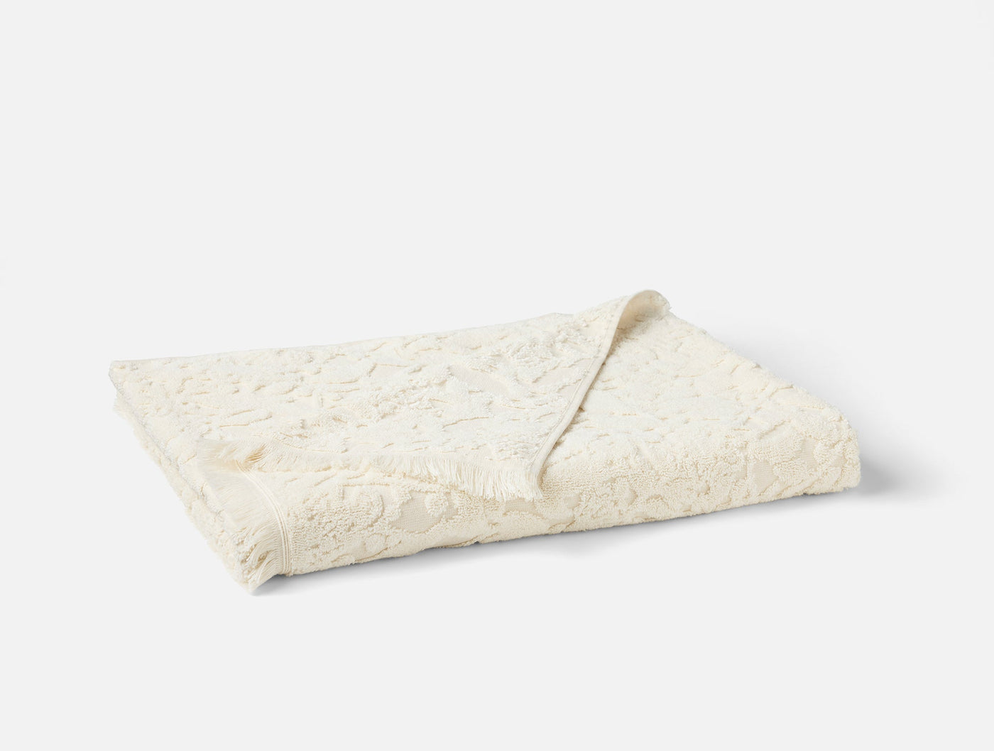 Close-up of folded ivory Coyuchi Wildflower bath towel showing floral texture detail.