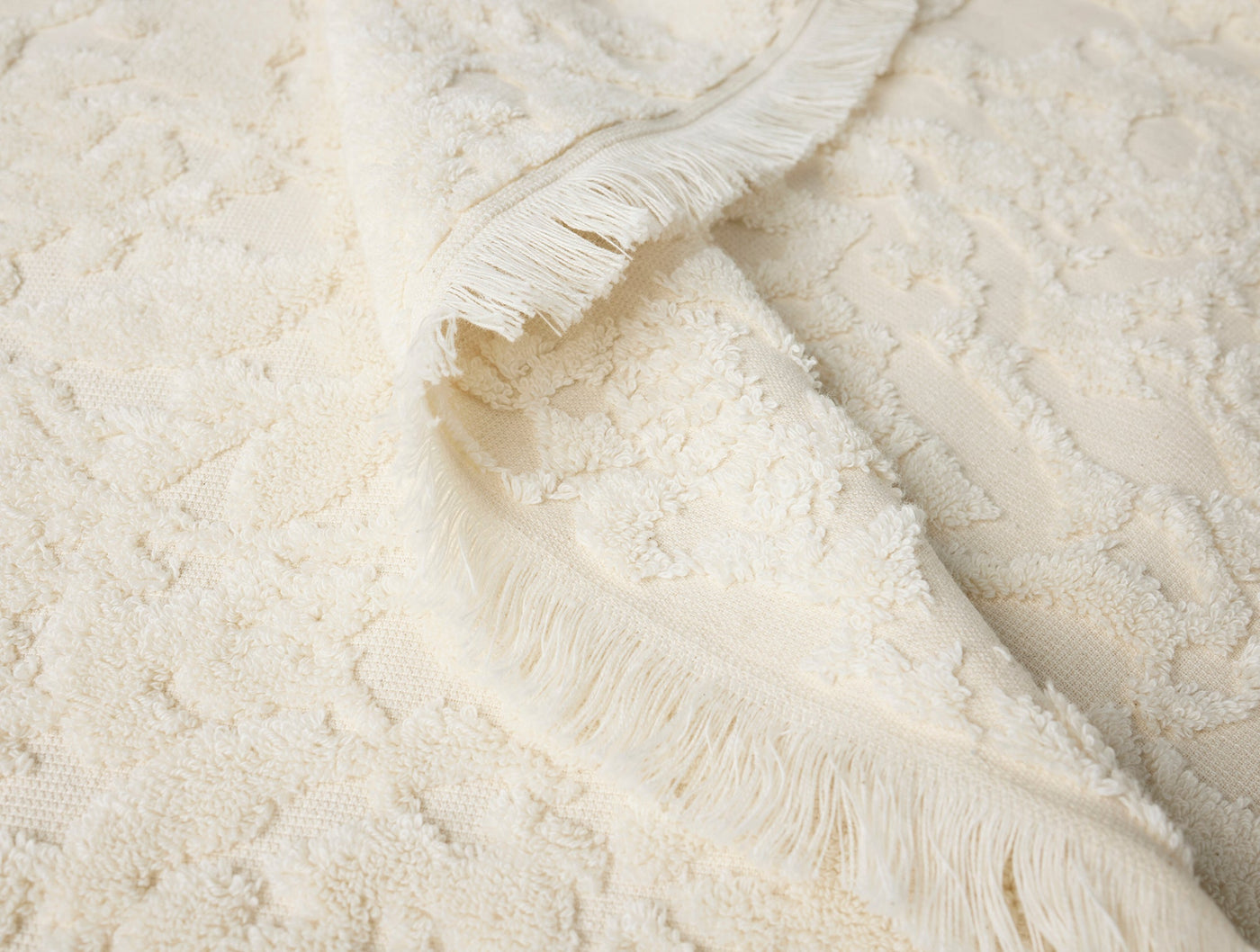Close-up of ivory Coyuchi Wildflower bath towel showing tufted texture and fringe edge detail.