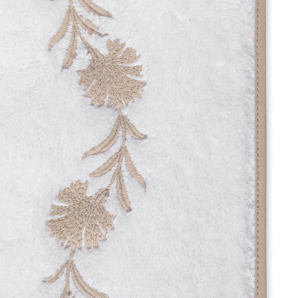 Close-up of champagne floral embroidered border on white terry bath sheet.