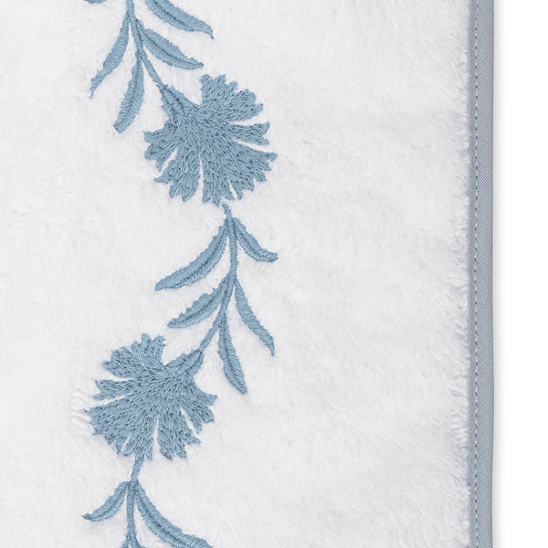 Close-up of slate blue floral embroidery along the border of a white terry bath sheet.