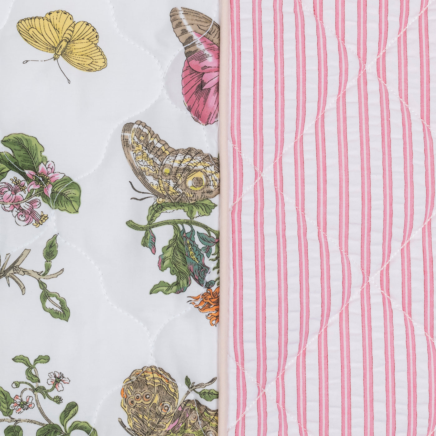 Close-up of the Matouk Reversible Quilted Lumbar Pillow Cover, featuring a butterfly and floral print on one side, pink and white stripes on the other, divided by a pink border—ideal for adding decorative flair.
