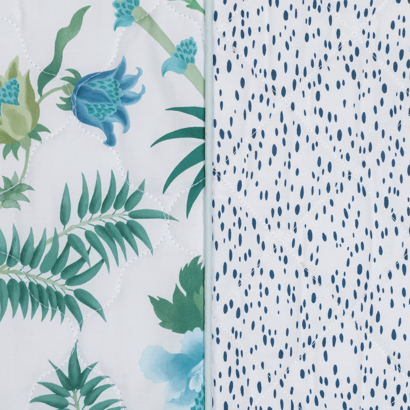 Close-up of two fabric patterns on the Matouk Reversible Quilted Lumbar Pillow Cover: one with green leaves and blue flowers, the other with small blue dots on white. A vertical seam separates the customizable sections.