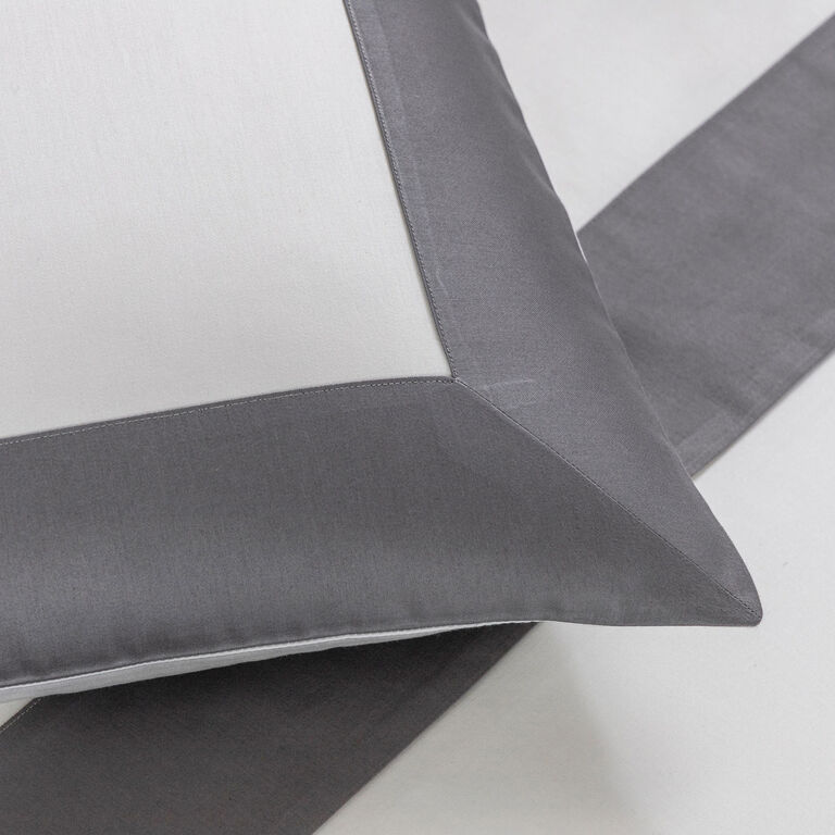 A close-up of a white pillowcase with a wide gray border, resting on matching bedding, adds a modern touch to any bedroom—part of the Bold | Sheet Set by Frette.