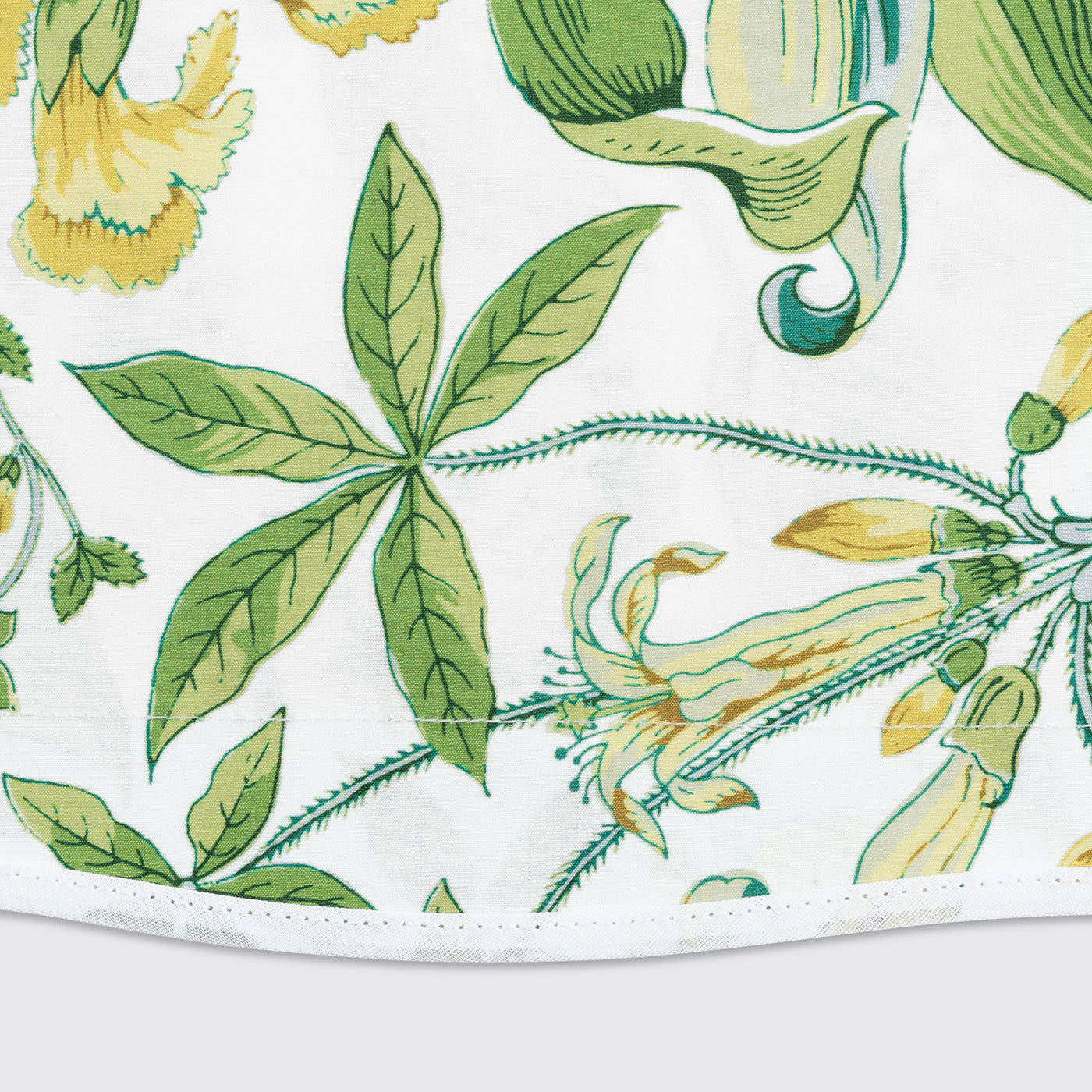 Close-up of green and yellow botanical print on white cotton, showing hemmed edge detail.