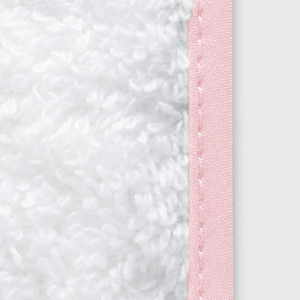 Close-up of white plush terry fabric with blush pink piped trim and whipstitch detailing.