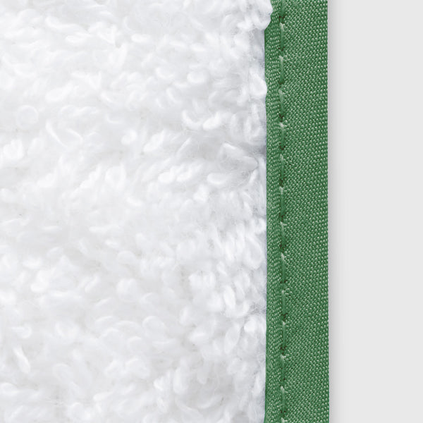 Close-up of white plush terry fabric with sage green ribbon piping detail.