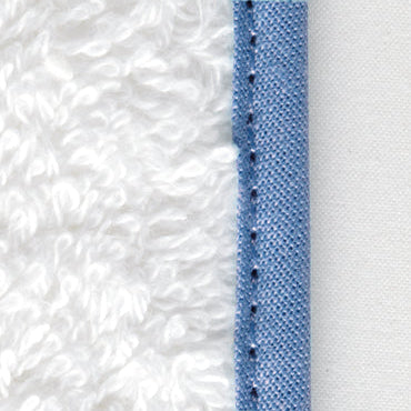 Close-up of periwinkle cotton piping seam joining white plush terry robe fabric.