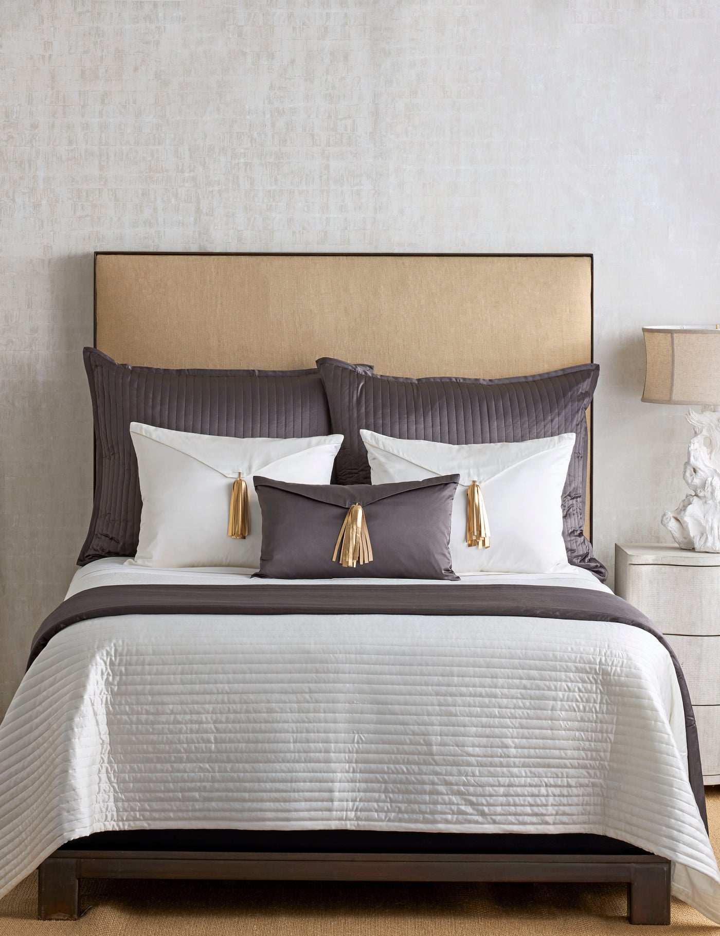 Ann Gish Saihai pillow in charcoal velvet with gold tassels, styled on a layered bed.