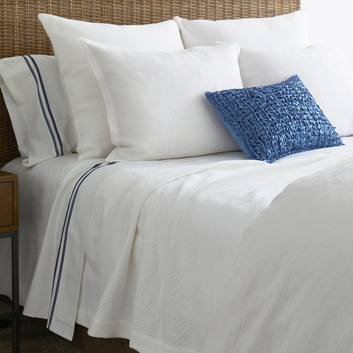 White matelassé duvet styled on bed with navy-striped pillowcases and blue textured accent pillow.