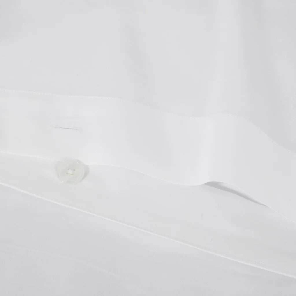 A close-up of a white button on smooth fabric, evoking the sleek, luxurious finish of the Frette Sateen | Duvet Cover by Frette.