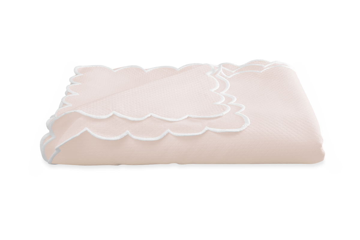 A folded Savannah Gardens tablecloth by Matouk in light pink diamond pique with white scalloped edges, displayed on a plain white background. Easy care for everyday comfort.
