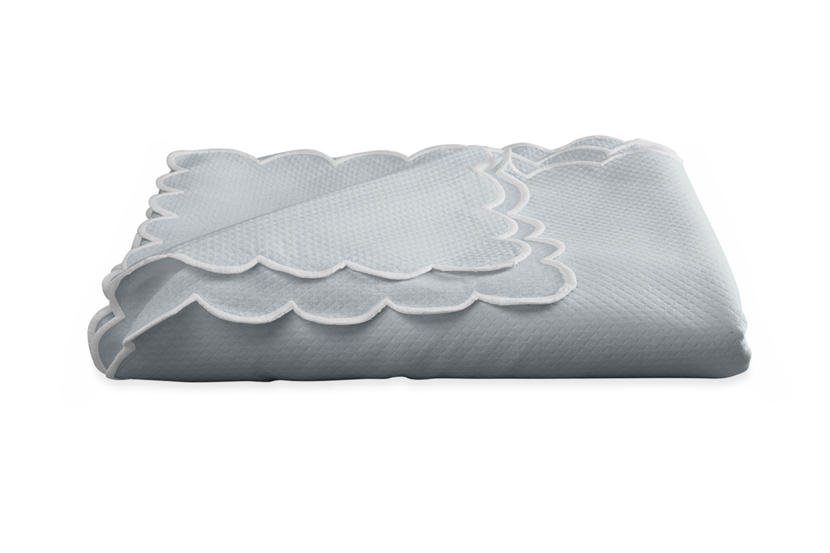 The Savannah Gardens tablecloth by Matouk features a light blue diamond pique design with scalloped edges, neatly folded on a white background for easy care and timeless style.