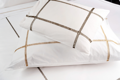 Close-up of white pillowcases with embroidered grid border in gold and charcoal.