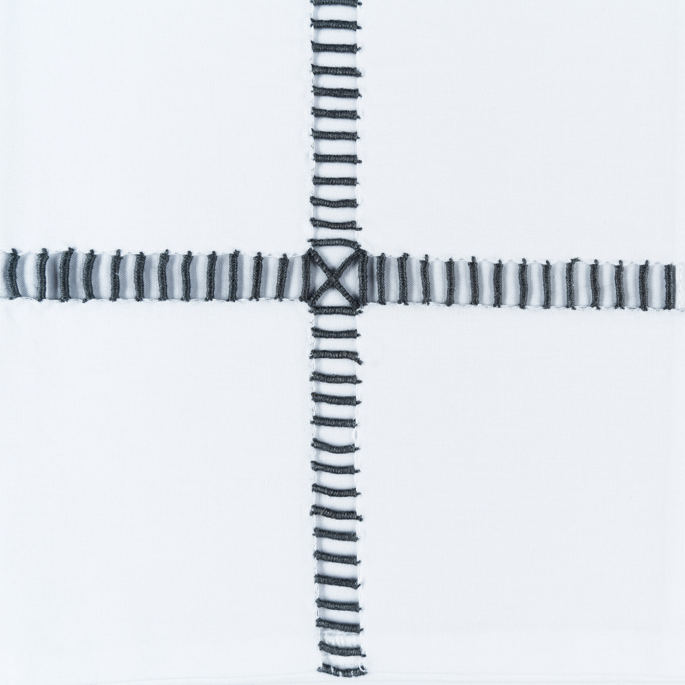 Close-up of charcoal hand-stitched cross detail on white linen fabric.