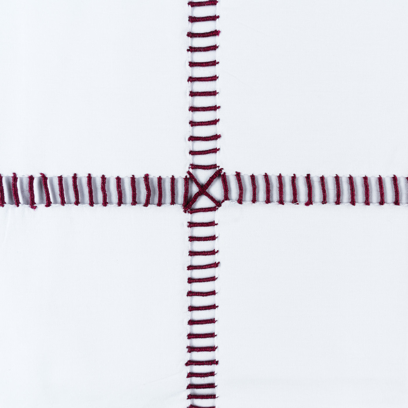Close-up of crimson hand-stitched cross detail on white linen, Henry Handwork Scala.