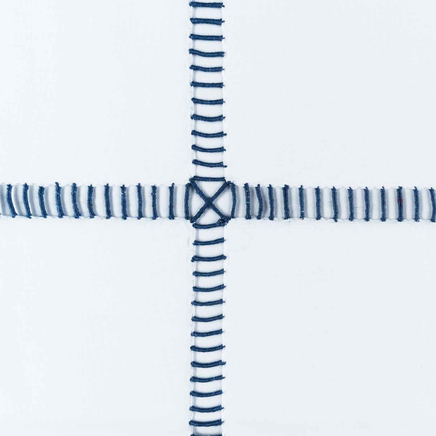 Close-up of navy hand-stitched grid embroidery with cross-stitch intersection on white linen.