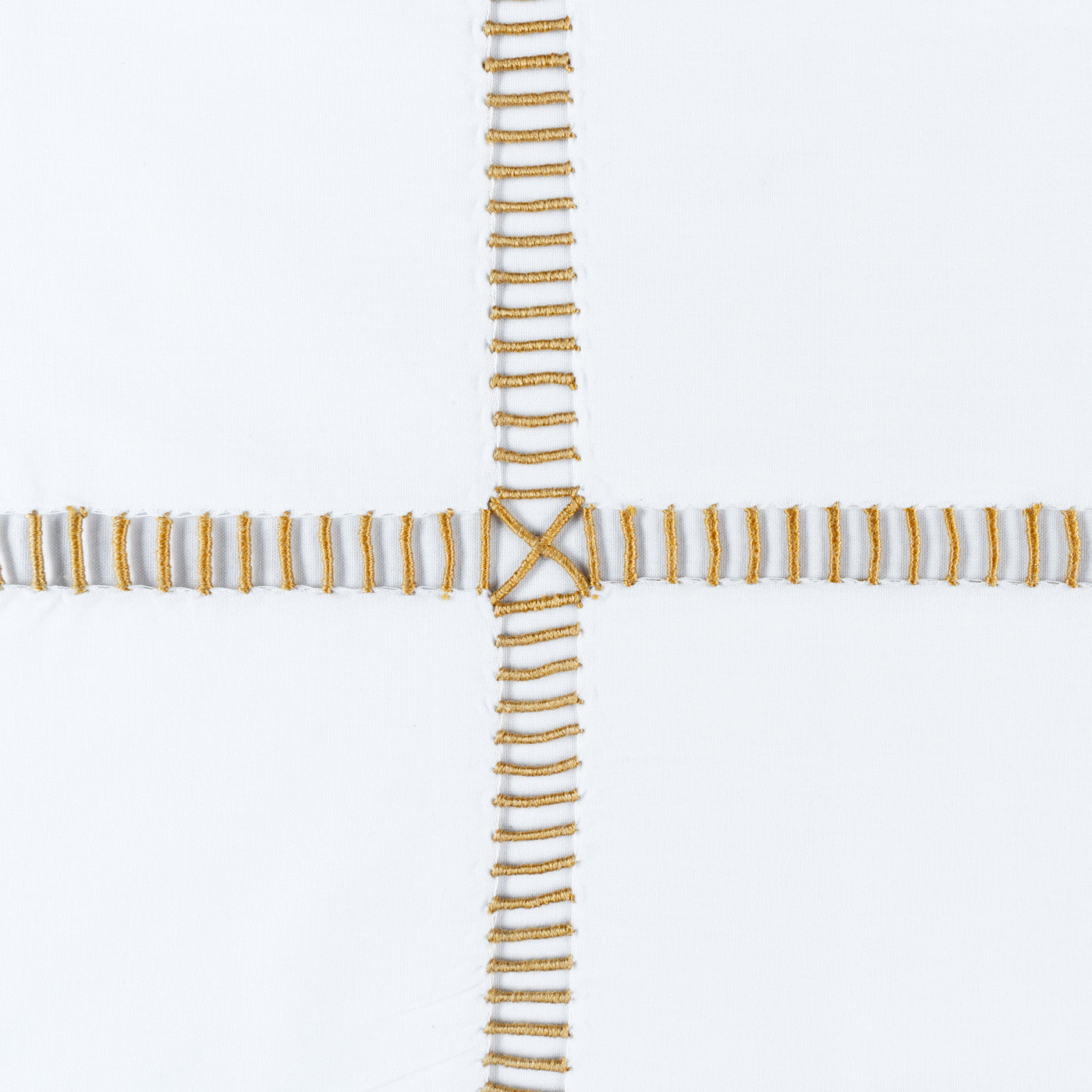 Close-up of gold ladder-stitch embroidery intersecting on white linen fabric.