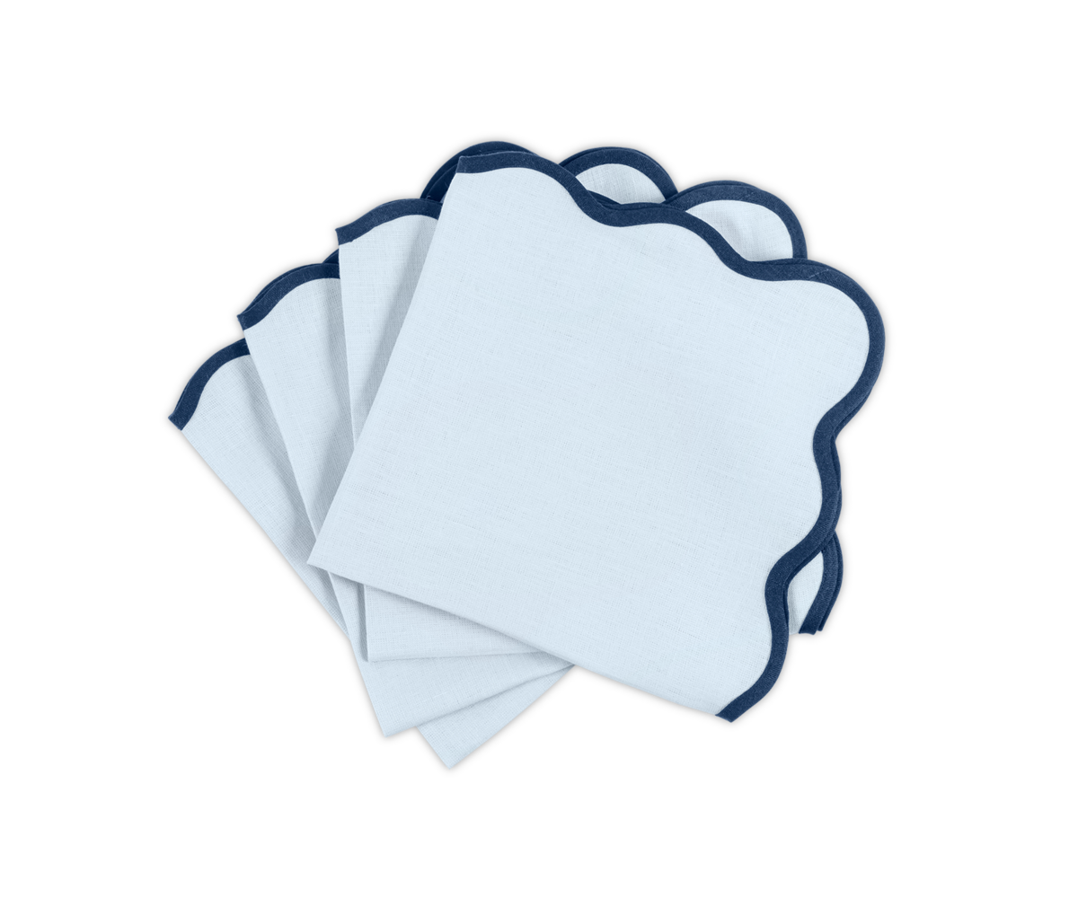 The Matouk Scallop Edge Napkin Set features four white napkins with navy blue trim, stacked on a white background—ideal for elevating your tablescape or pairing with linen placemats.