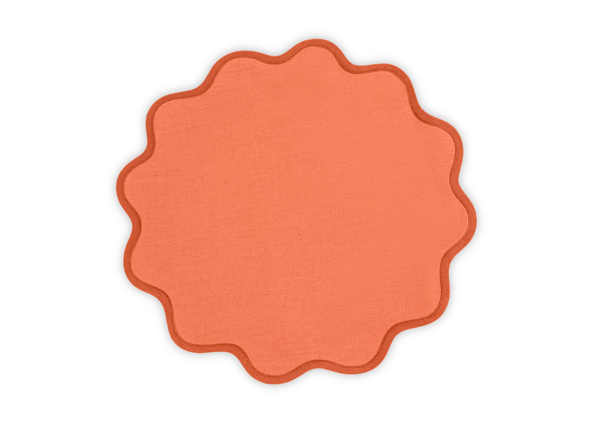 The Matouk Scallop Edge Placemat Set features round, orange linen placemats with wavy scalloped edges, providing a unique accent to any tablescape.