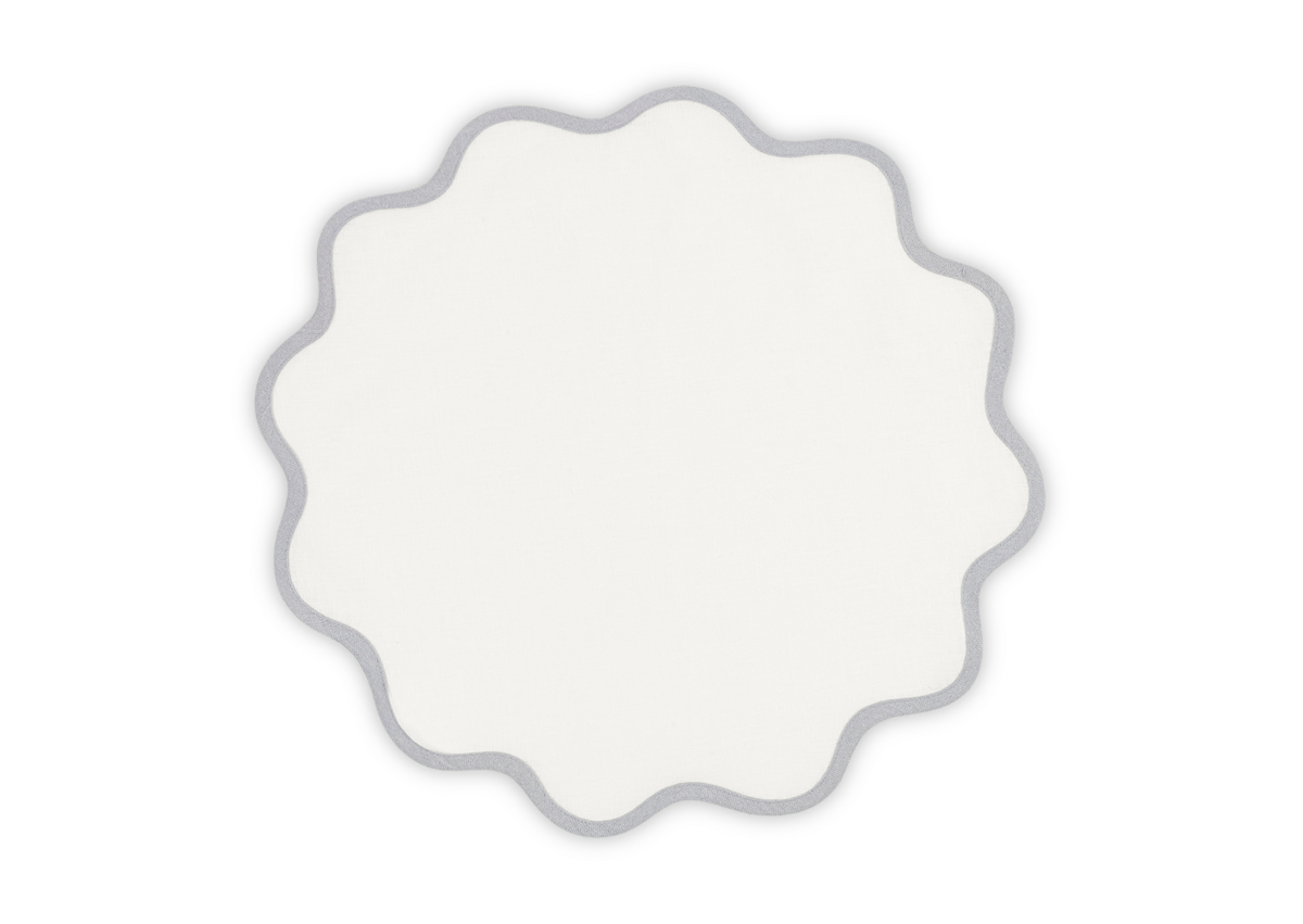 The Scallop Edge Placemat Set by Matouk features white circular linen placemats with wavy gray-outlined edges, ideal for adding a unique touch to your tablescape.