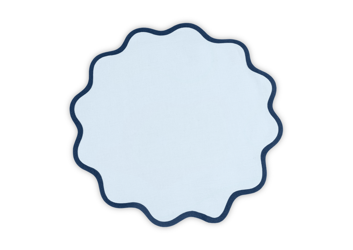 The Scallop Edge Placemat Set by Matouk features round white linen mats with wavy dark blue edging, perfect for a unique tablescape. Shown against a light background.
