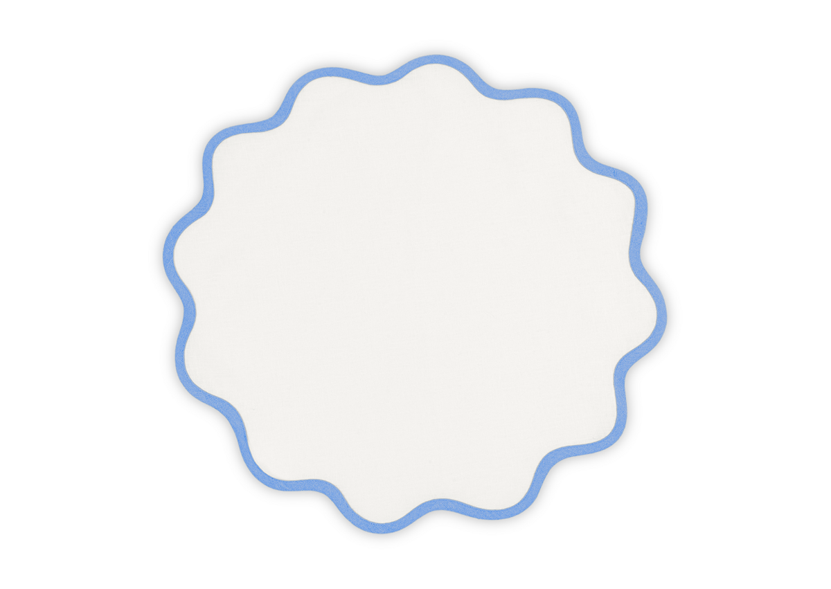 The Matouk Scallop Edge Placemat Set, featuring white round linen with wavy blue-outlined edges, is displayed on a plain light background—ideal for adding a unique touch to your tablescape.