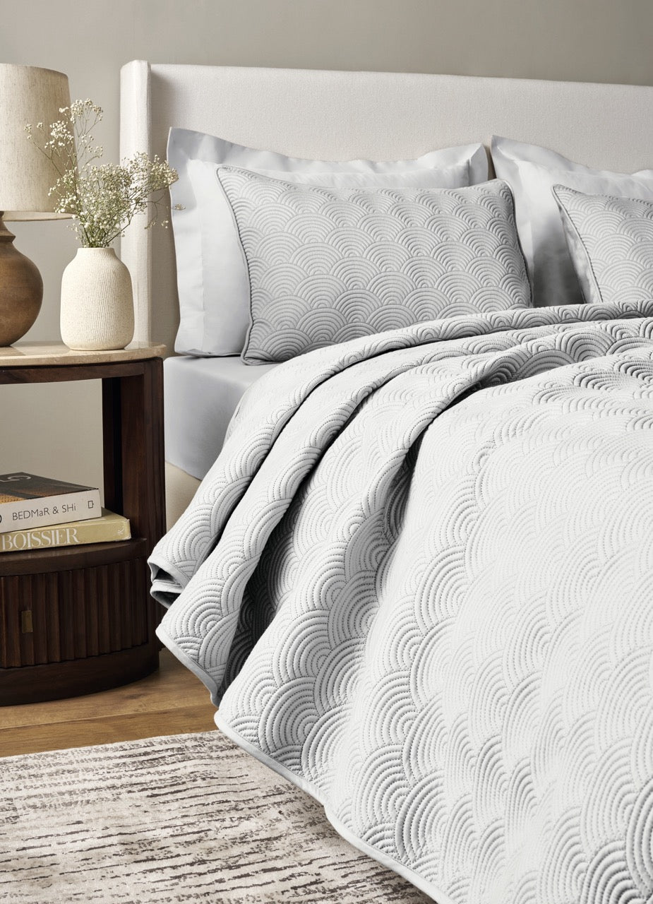 White Ann Gish Scallop coverlet set with embossed arc quilting, styled on bed with grey shams.