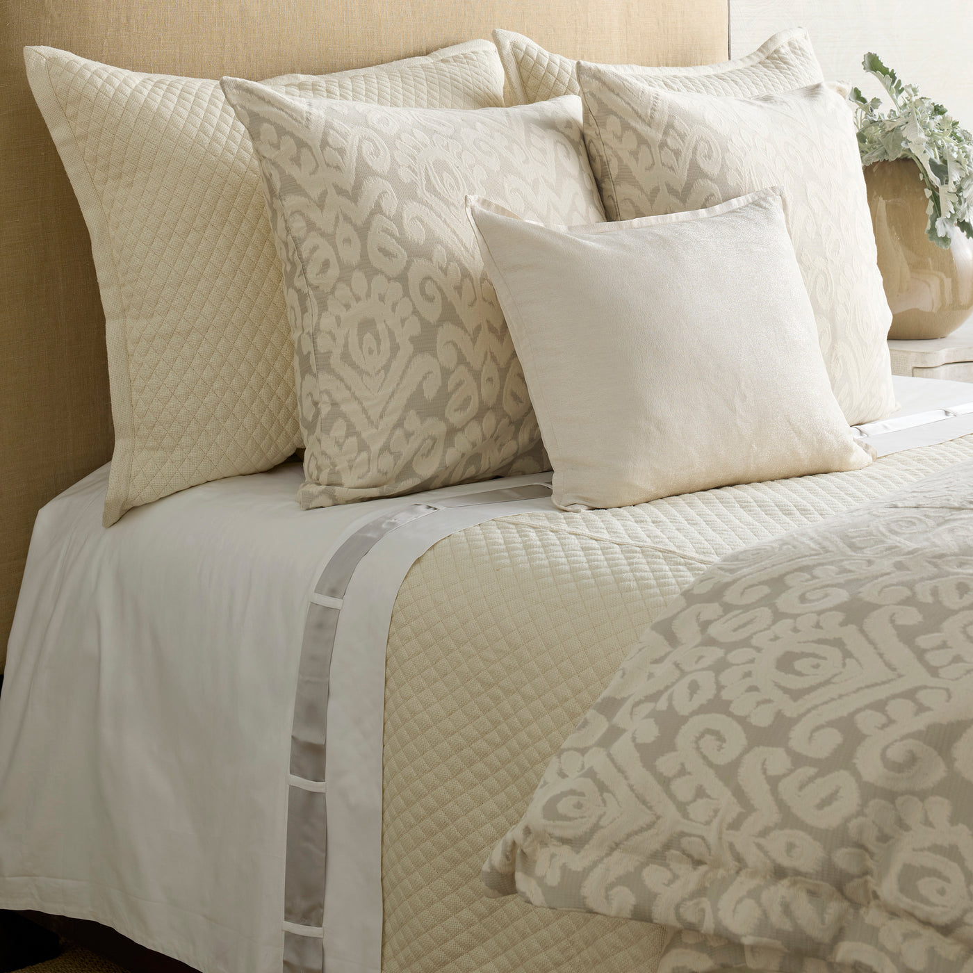 Ivory and champagne ikat-patterned duvet with quilted shams styled on a made bed.