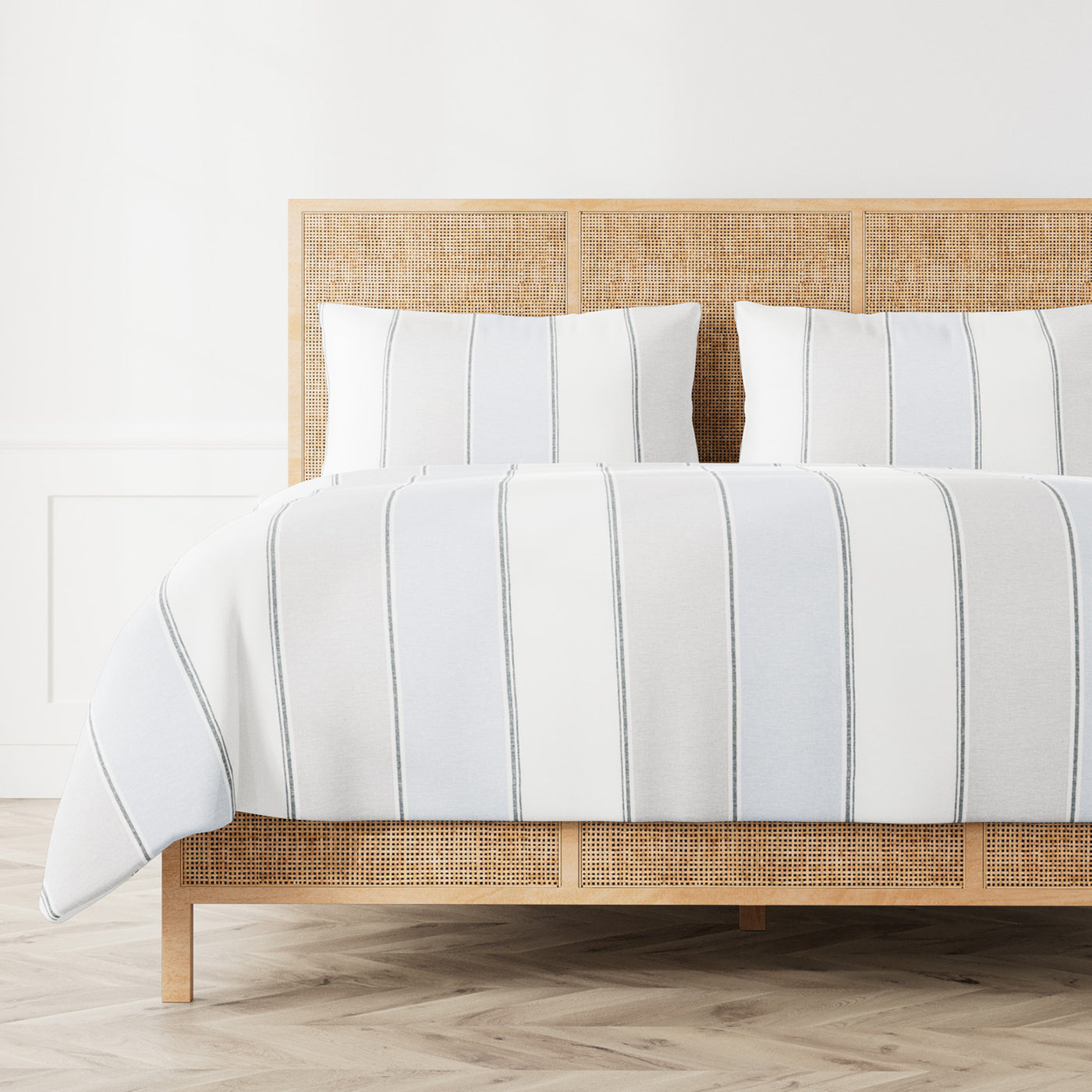 Ann Gish Schooner duvet set in white with charcoal vertical stripes on a rattan bed.