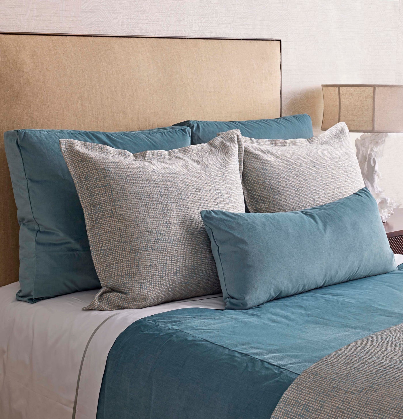 Teal coverlet and pillow shams styled with stone linen pillows on a neutral bed.